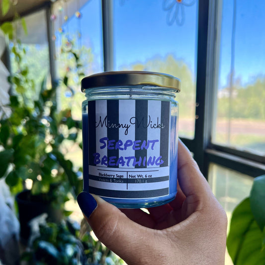 Hand holding a candle labeled 'Serpent Breathing' in front of a window with plants in the background