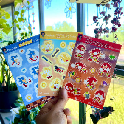 Three sonic sticker sheets held by a hand in front of a window with plants