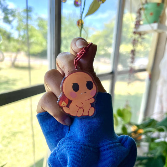 Hand holding a small keychain with a cartoon character in front of a window with outdoor view